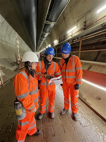 Three people wearing work overalls, standing in a tunnel